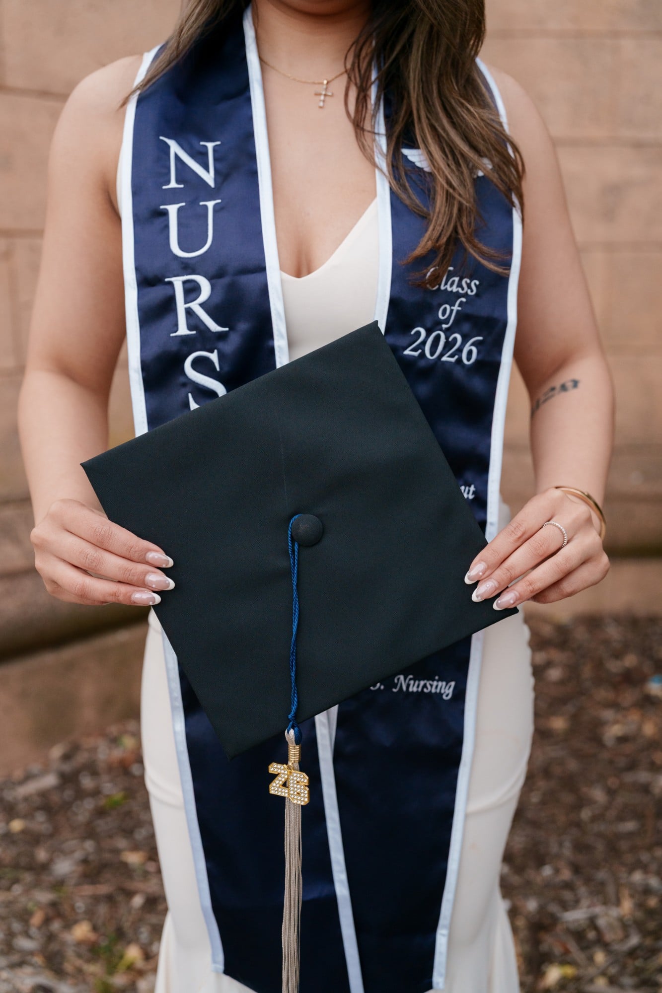 Close-up of nursing grad holding black mortarboard showing navy SMU Nursing stole and gold Class of 2026 tassel charm