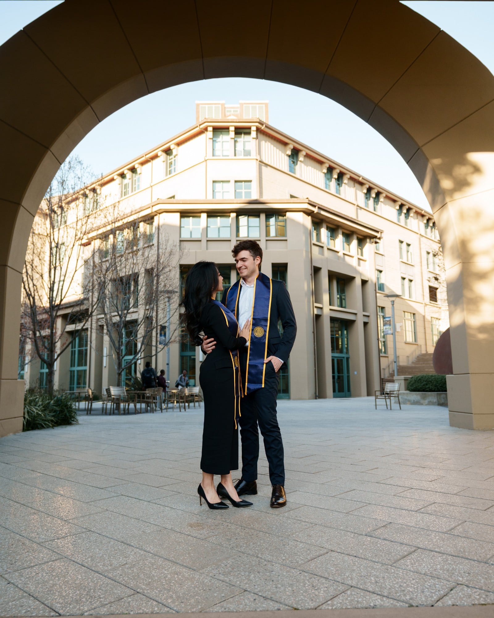 UC Berkeley grad couple facing each other under a stone archway with Haas School of Business building glowing in warm afterno